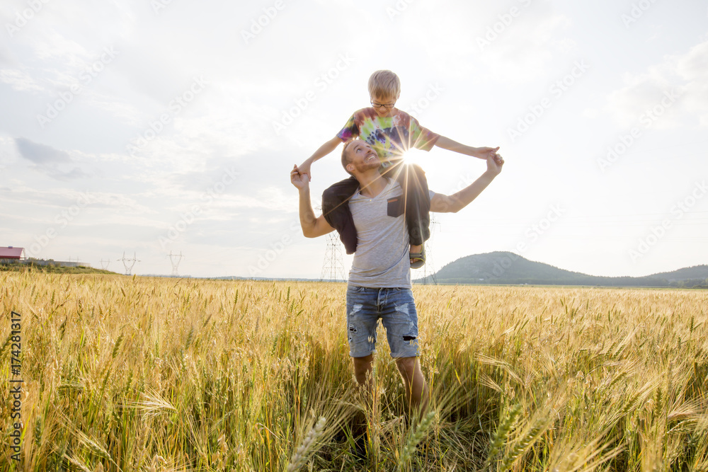 young father with his little son walking in the wheat field at sunset in a warm summer day young father with his little son walking in the wheat field at sunset in a warm summer day