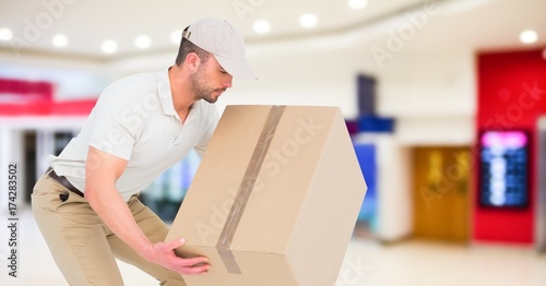 Delivery man picking up box against blurry shopping centre