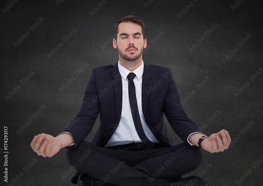 Business man meditating against grey wall Business man meditating against grey wall