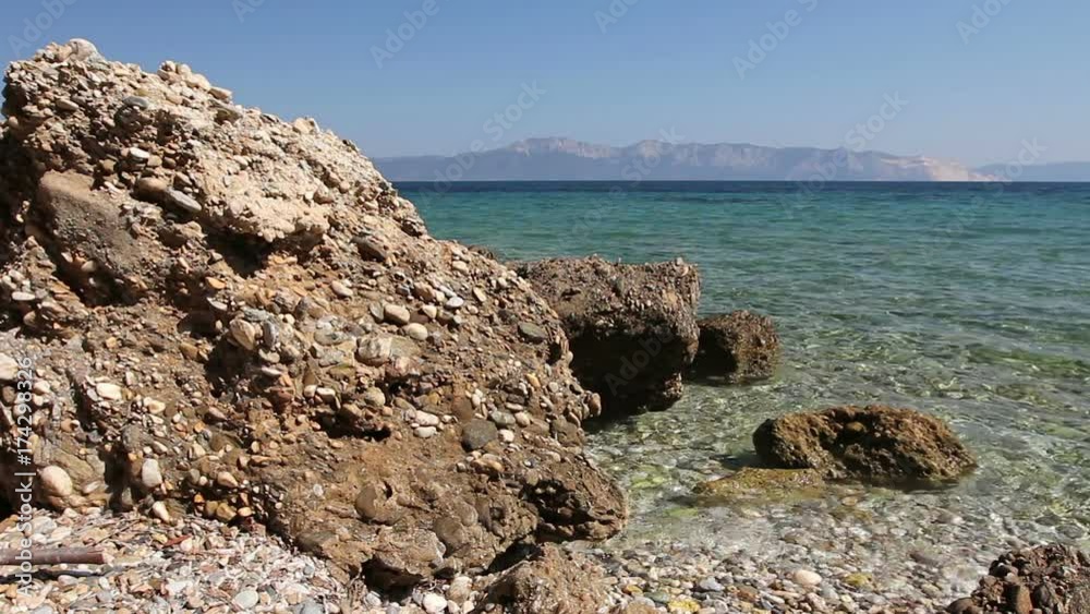 Rocky shore with boulder sticking out of shallow water surface with mountain coast in the background Rocky shore with boulder sticking out of shallow water surface with mountain coast in the background