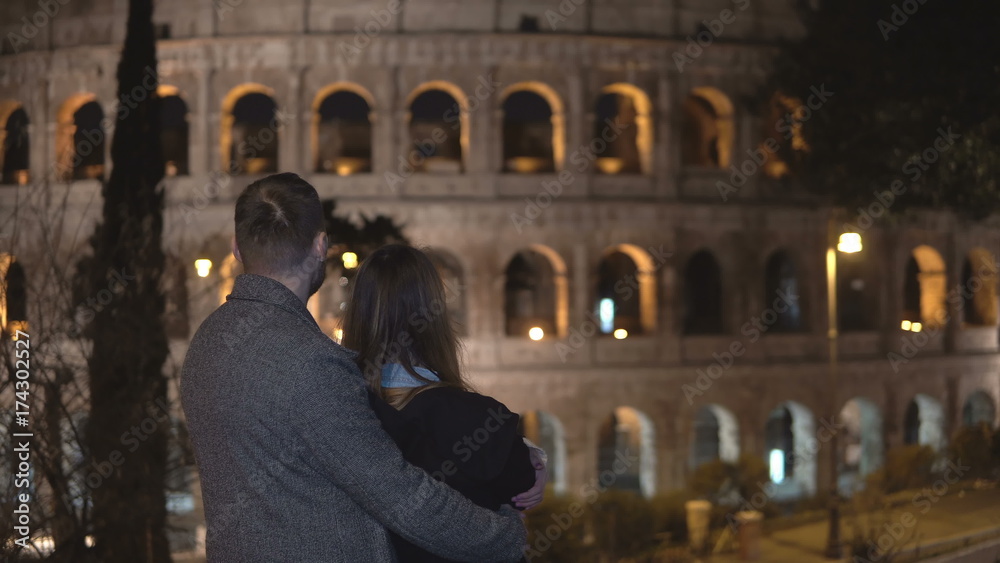 Back view of young man and woman standing near the Colosseum in Rome, Italy and hugging together.