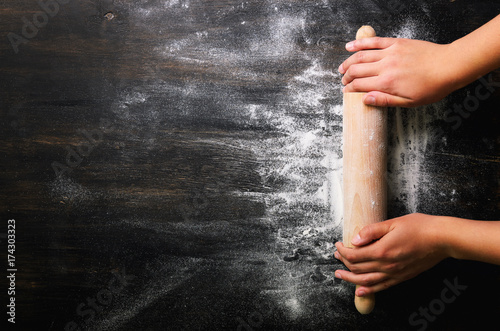 Girl hands keep rolling pin with flour on dark black table, baking background, top view, copy space for your text, meru, recipe. Banner