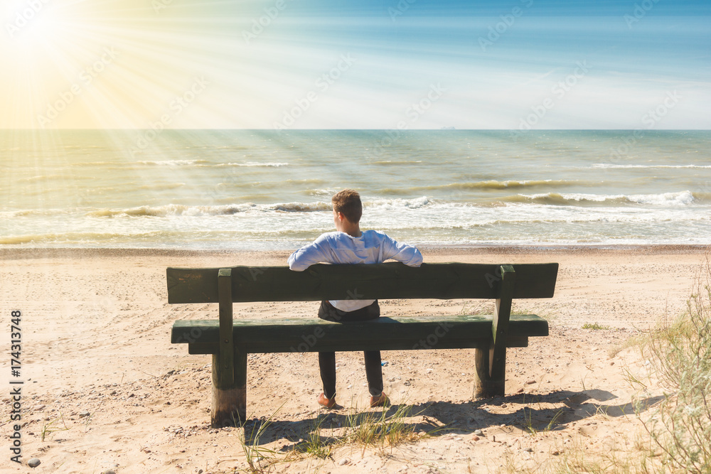 young man sitting on a lonely bench on the sea shore 