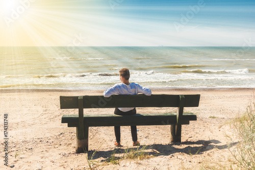 young man sitting on a lonely bench on the sea shore 