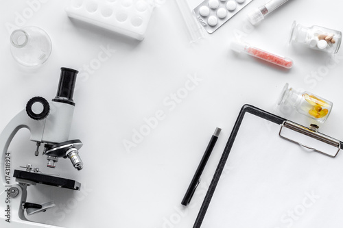 Doctor's workplace. Microscope, tablet, pills and test tube on white background top view copyspace