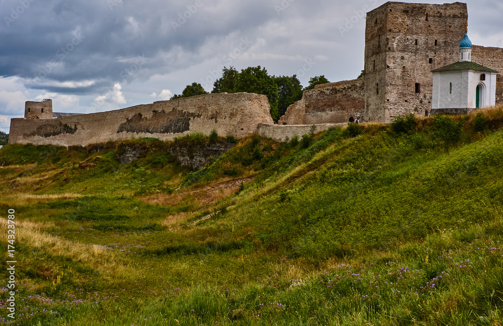 Fortress wall on the hill/On the hill there is an ancient fortress. The wall is partially destroyed. Near the square watchtower is a white Orthodox chapel. Russia, Pskov region, landscape
