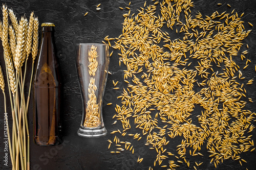 Grains and ears of malting barley near beer bottle on black background top view