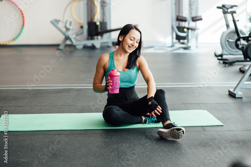 Young woman drinking water in gym, photo