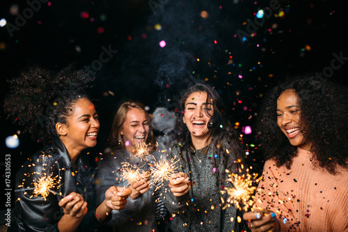 Happy women at night. Laughing friends with sparklers under confetti. photo