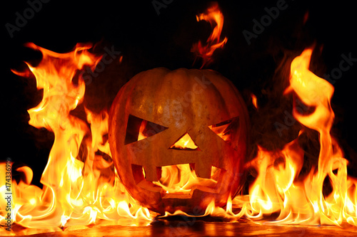 The concept of Halloween. The evil terrible pumpkin is burning in the hellish tongues of flame. Jack Lantern in the middle of the fire