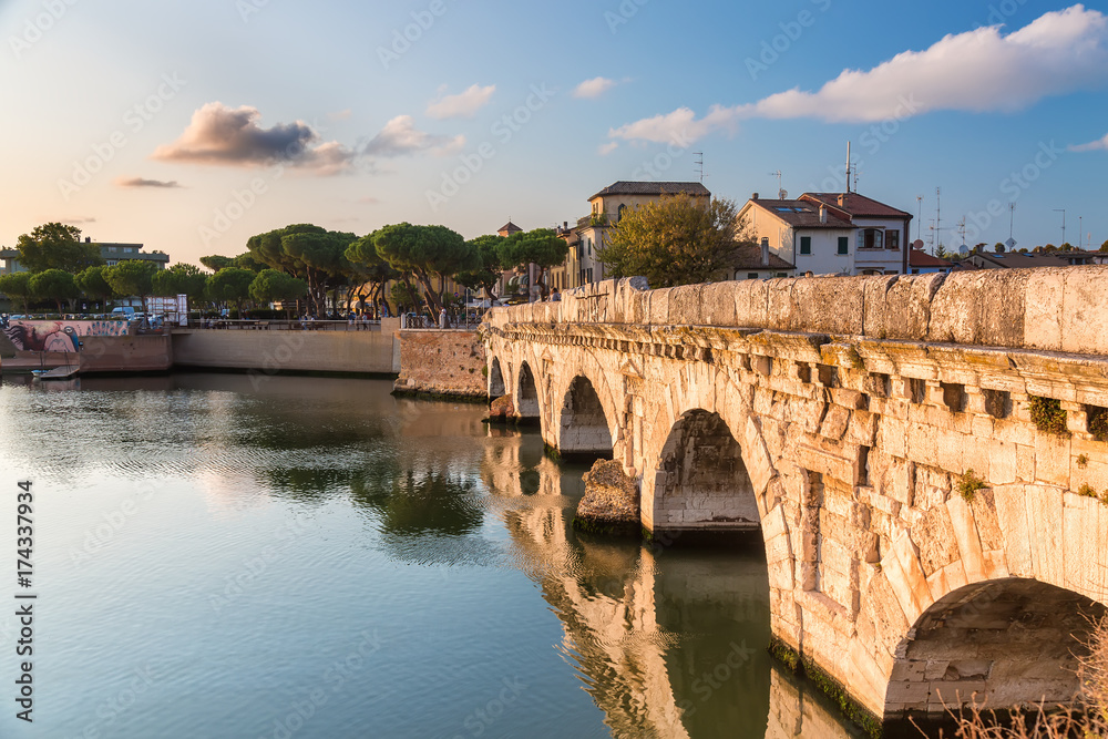 Historical roman Tiberius bridge over Marecchia river during sunset in Rimini, Italy.