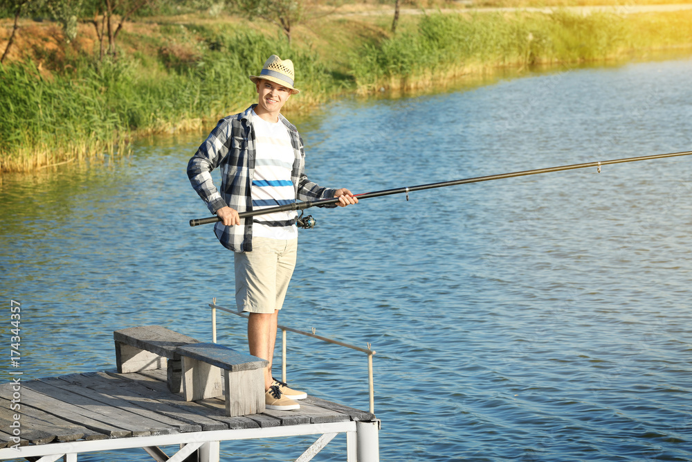 Young man fishing from pier on river Young man fishing from pier on river