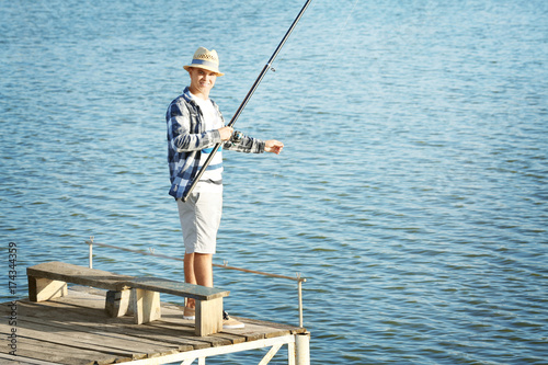 Young man fishing from pier on river