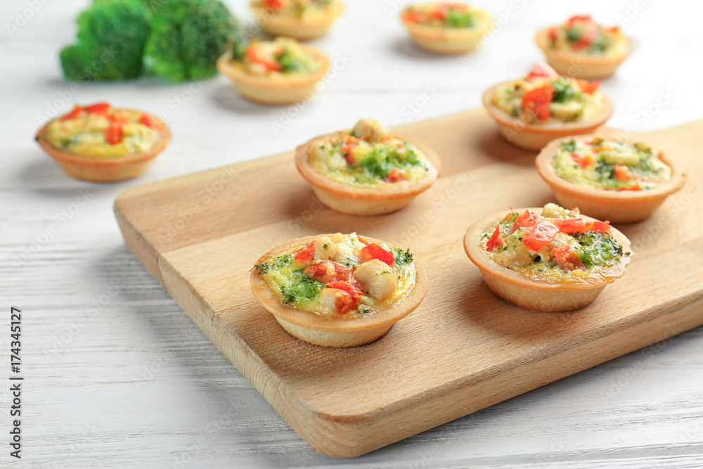 Board with broccoli quiche tartlets on table