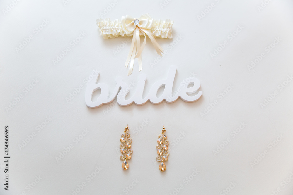 Earrings and garter of the bride with word bride lie on the white table Earrings and garter of the bride with word bride lie on the white table