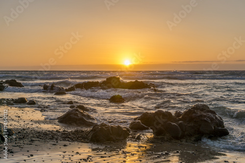 sunrise on a beach with waves and stones in the water