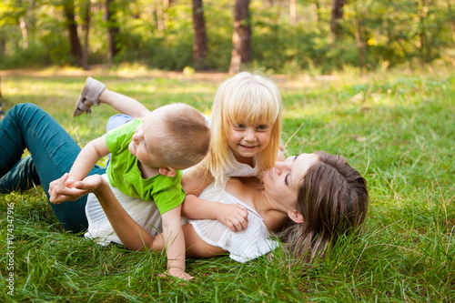 Family concept, mother and her daughter and son together playing and laughing on the grass