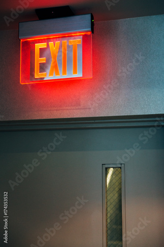 A red exit evacuation light up neon sign above a door inside a building