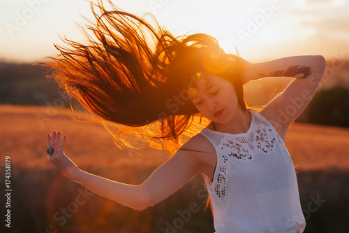 A brunette woman with her hair thrown to one side, backlit by the sunset photo
