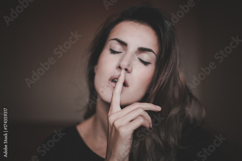 Girl with closed eyes making shhh sign with focus on her hand photo