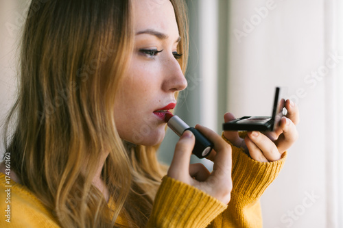 Beautiful woman applying red lipstick in front of a mirror. photo