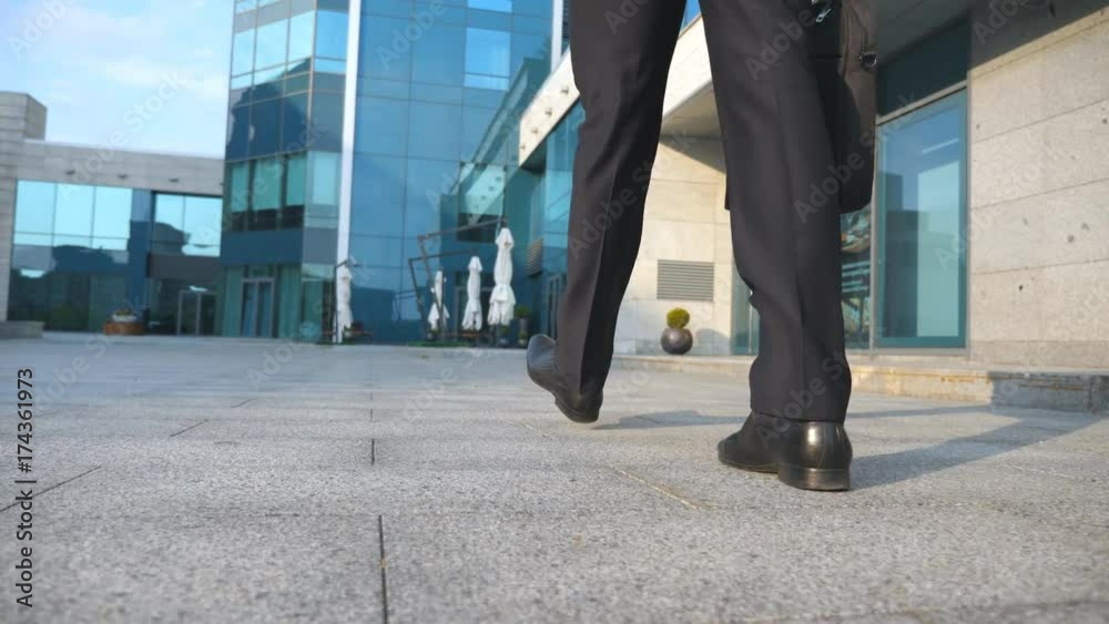 Business man commuting to work. Confident guy in suit being on his way to office building. Young businessman with a briefcase walking in city. Slow motion Rear back view Close up Business man commuting to work. Confident guy in suit being on his way to office building. Young businessman with a briefcase walking in city. Slow motion Rear back view Close up