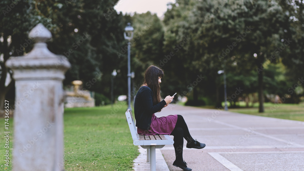 Woman using a smart phone in a city park sitting on a bench Woman using a smart phone in a city park sitting on a bench