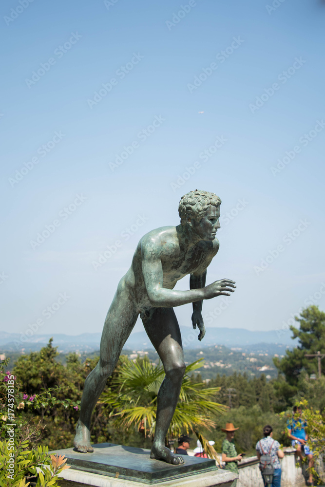 Fototapeta premium An antique sculpture of a man standing behind a background of blue sky and mid-ocean trees