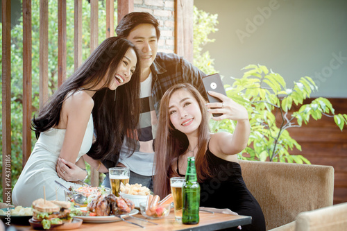 Young Asian peoples are selfie together on a day of party. On the table, there are many beer and food.