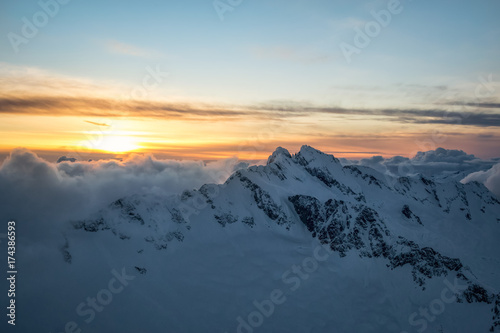 Dreamy aerial landscape view of the beautiful snow covered mountains during a cloudy sunset. Picture taken of Tentalus Range near Squamish, British Columbia, Canada.