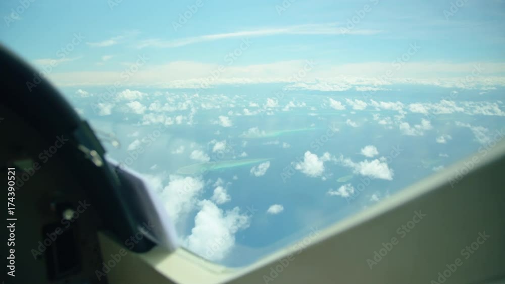 A still shot of the blue sea and sky from a moving airplane. Corals are seen in the shot.