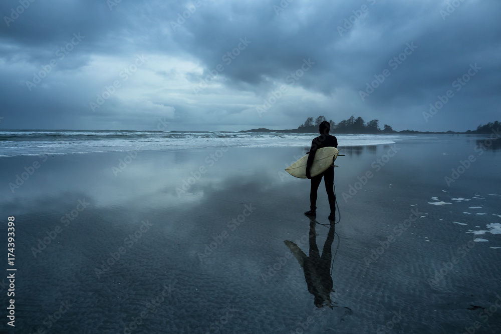 Surfer heading out in the ocean during a cloudy winter sunset. Picture taken in Chesterman Beach, Tofino, Vancouver Island, BC, Canada.
