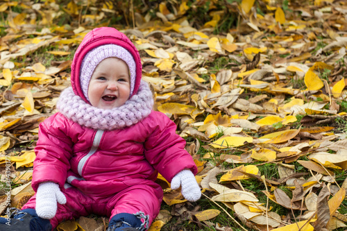 Happy little baby girl in pink jumpsuit  white mittens and pink scarf having fun in the autumn park