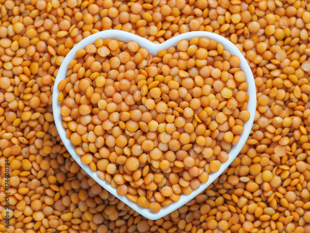 Red orange lentil Football in heart bowl on lentils background Red orange lentil Football in heart bowl on lentils background