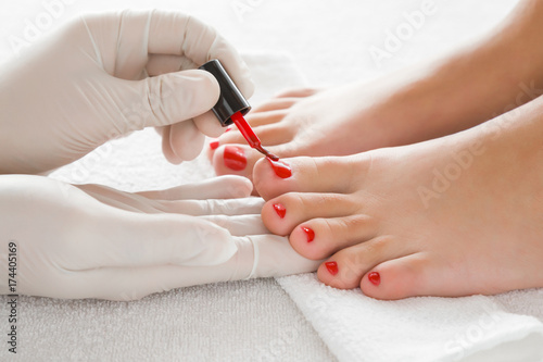 Hands in gloves cares about a woman's foot nails. Pedicure, manicure beauty salon concept. Nail varnishing in red color.