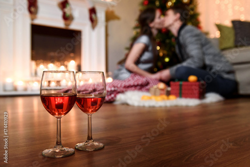 Two glasses of sparkling wine in front of warm fireplace. Cozy relaxed romantic atmosphere near fire of fireplace. A close picture of two wine glasses and a warm blurred kiss on the background.