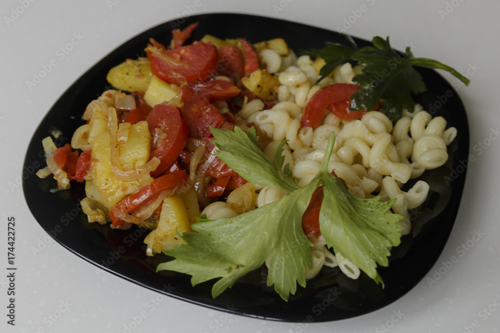Pasta with stewed vegetables on a black dish isolated on a white background Pasta with stewed vegetables on a black dish isolated on a white background