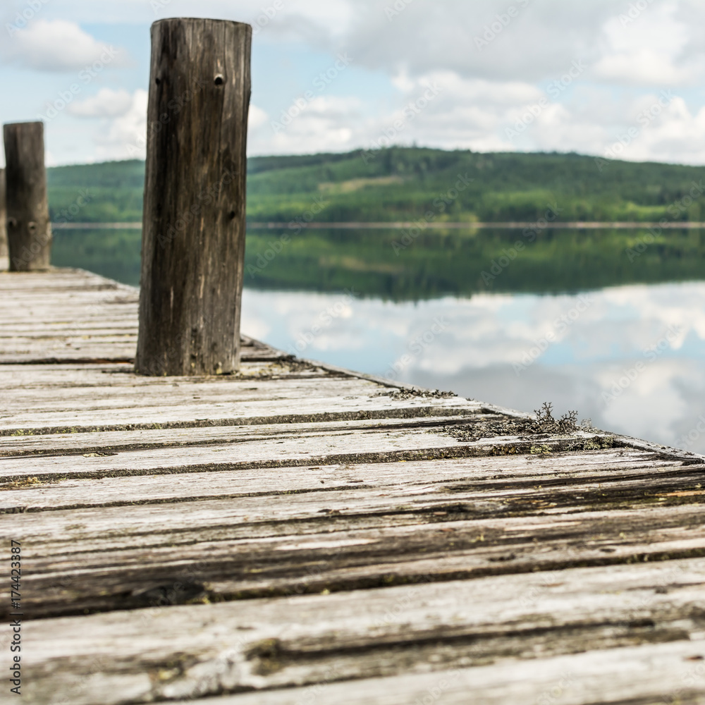 Old wooden pier on calm lake with reflection of mountains and cloudy sky. Dalarna region, Sweden