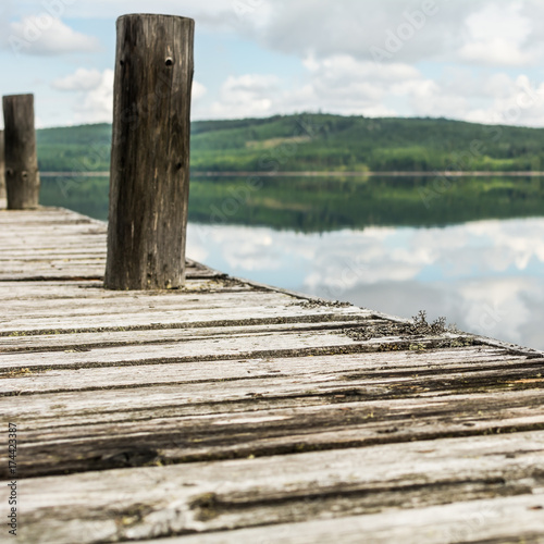 Old wooden pier on calm lake with reflection of mountains and cloudy sky. Dalarna region, Sweden