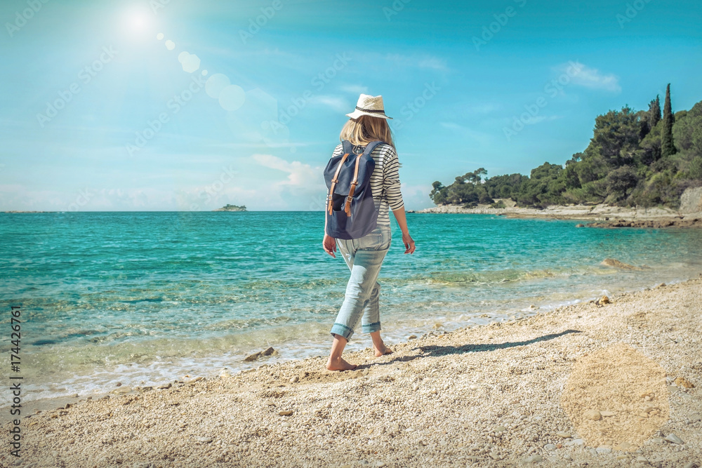 Blonde woman in summer hat with her backpack walking in the sand