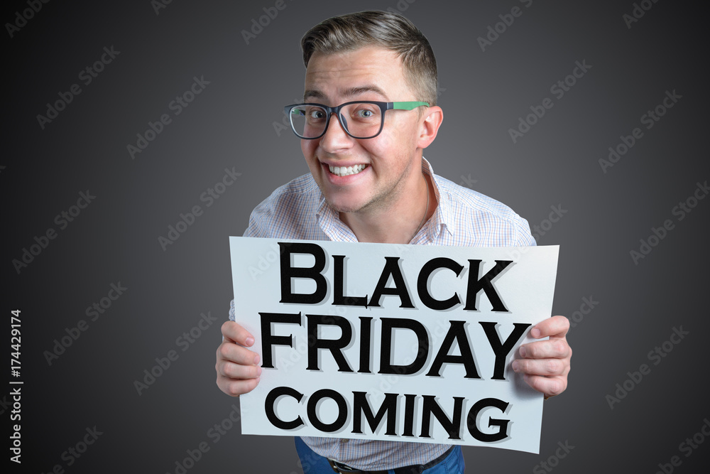 Funny laughing guy (men, student, businessman) of european appearance in casual clothes and glasses is holding a white sheet with text Black friday coming! Funny laughing guy (men, student, businessman) of european appearance in casual clothes and glasses is holding a white sheet with text Black friday coming!