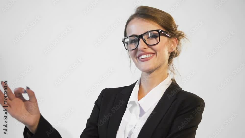 Happy young dark hair caucasian businesswoman, in a white blouse and a black jacket, is showing OK in the white background, isolated, slow motion Happy young dark hair caucasian businesswoman, in a white blouse and a black jacket, is showing OK in the white background, isolated, slow motion