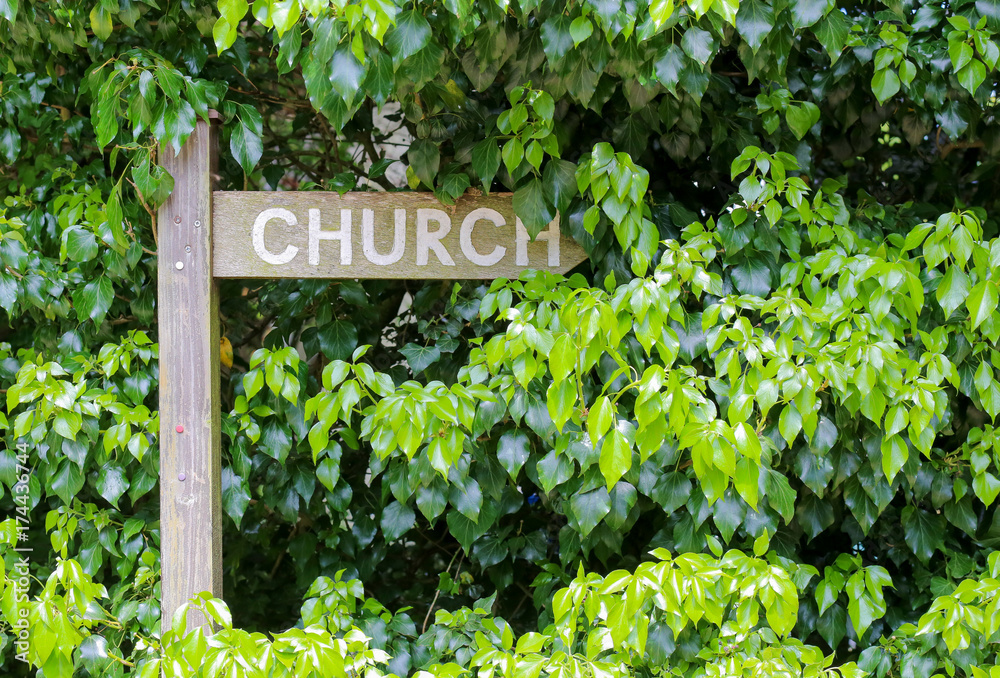 Overgrown wooden signpost for church way with green hedge background