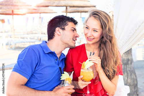 Happy couple of young lovers drinking cocktails on a beach bar at sunset - Concept of summer , holidays , relax