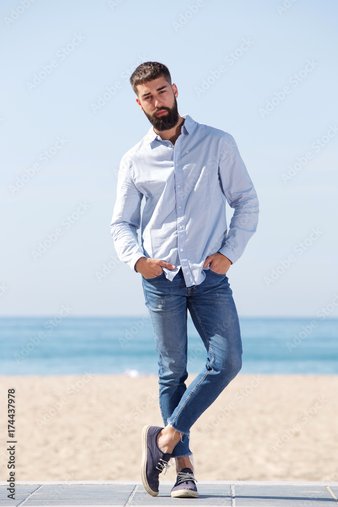 Full length serious handsome man standing by beach posing Full length serious handsome man standing by beach posing