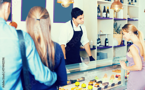 Adult seller helping friends to choose sweets photo