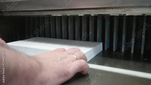 White man adjusts a pack of white paper in guillotine cutter before cutting photo