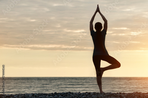 Girl at sunset practicing yoga at the seashore, back view © somemeans