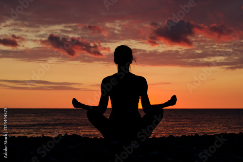 Woman meditating on the beach in lotus position. Silhouette, sunset