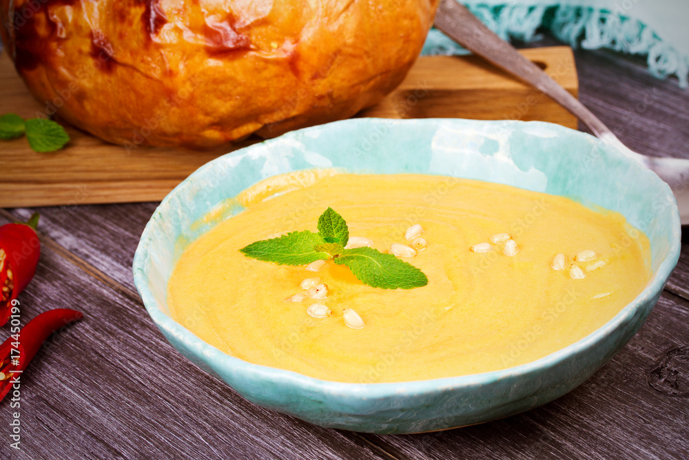 Creamy pumpkin (or butternut squash) soup in a bowl, whole roasted pumpkin on wooden background, horizontal Creamy pumpkin (or butternut squash) soup in a bowl, whole roasted pumpkin on wooden background, horizontal